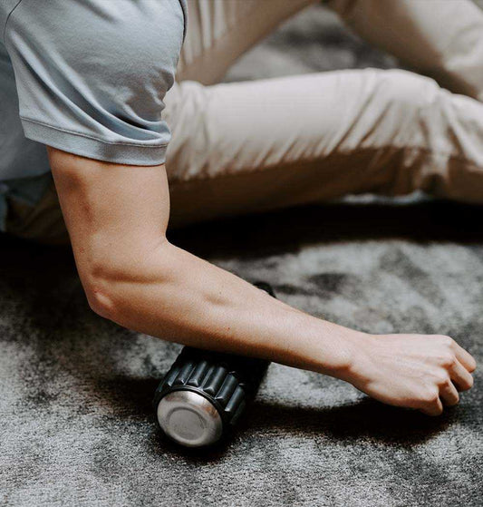 Mężczyzna używa wałka do masażu na podłodze, relaksując mięśnie po treningu.