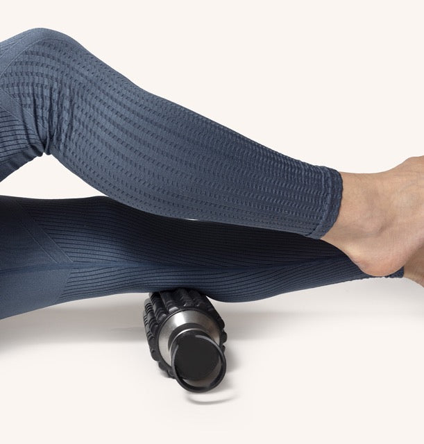 Stylowe legginsy z zaprezentowaną butelką na wodę 2w1 z wałkiem do masażu na tle stonowanej powierzchni.